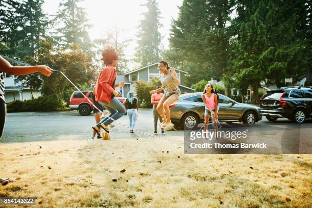 Group of teenage friends jumping rope together in front yard on summer evening
