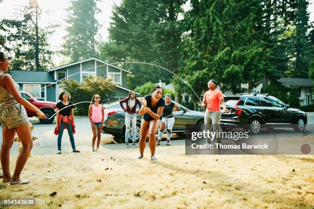 Laughing young woman trying to double dutch jump rope with friends on summer evening