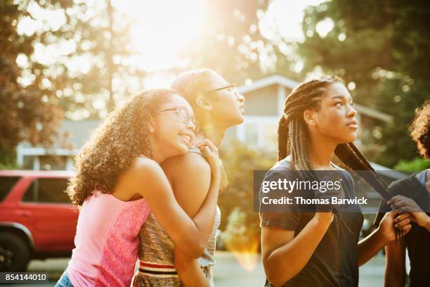 teenage girl embracing friend while hanging out in neighborhood on summer evening - young asian friends hugging stock-fotos und bilder