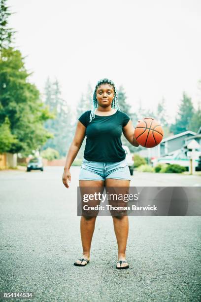 portrait of young woman dribbling basketball on neighborhood street - basketball portrait stockfoto's en -beelden