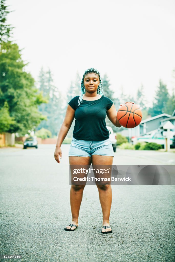 Portrait of young woman dribbling basketball on neighborhood street