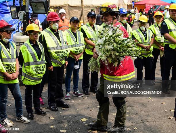 Firefighter carries a bunch of flowers he received from a woman as homage to their efforts in front of a line of rescuers, near the site where they...