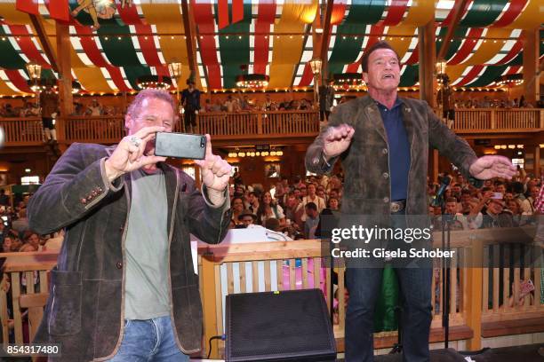 Arnold Schwarzenegger conducts the orchestra and Ralf Moeller photographs during the Oktoberfest at Schuetzen Festzelt at Theresienwiese on September...