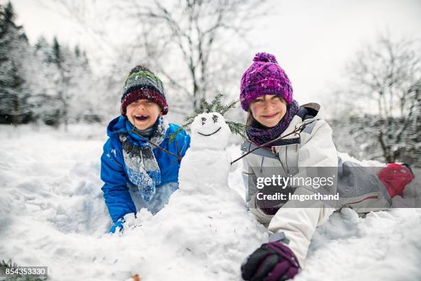 brother and sister building snowmen on a winter day - snowman building stock pictures, royalty-free photos & images