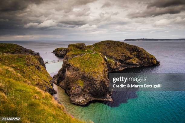 tourists crossing the carrick-a-rede rope bridge, northern ireland - ballycastle stock pictures, royalty-free photos & images