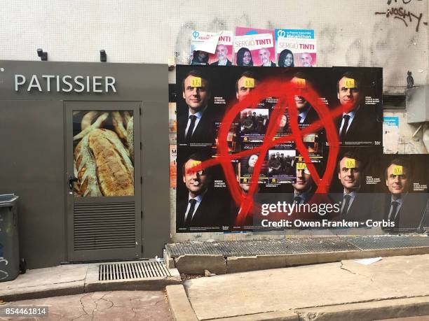Series of posters displaying the portrait of French President Emmanuel Macron are daubed with a circle-A alongside a bakery in the 19th...