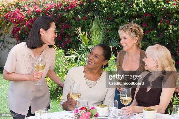 female friends drinking wine at outdoor table - four people smiling foto e immagini stock