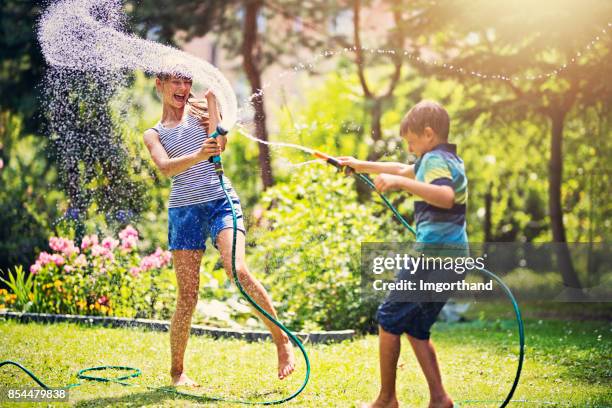 niños divirtiéndose de la manguera de jardín en el patio trasero - manguera fotografías e imágenes de stock