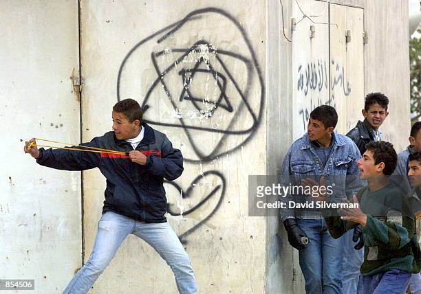 Urged on by his friends, a young Palestinian slings stones at Israeli troops during clashes December 4, 2001 by the Qalandia refugee camp in the West...