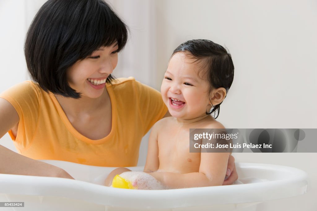 Asian mother washing her daughter in bathtub