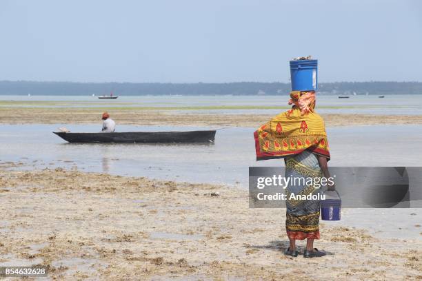 Tanzanian woman with a bucket on her head stands in water as a man sits on a fishing boat in Zanzibar, Tanzania on September 26, 2017. Tanzania's...