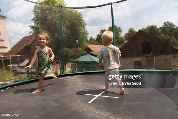 girl and a boy run around on trampoline in home's backyard. - family sports centre laughing stock-fotos und bilder