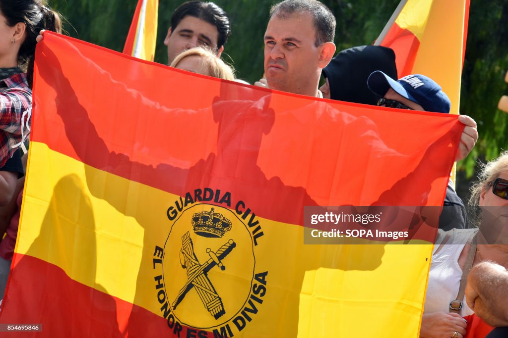 A man displays a flag of Spain with the coat of arms of the...