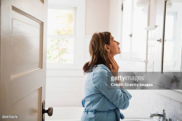 woman looking in bathroom mirror, touching neck - badkamer huis stockfoto's en -beelden