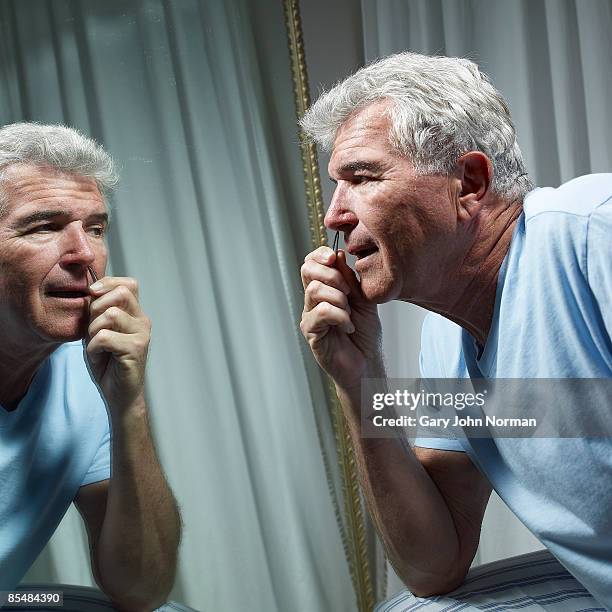 senior man with tweezers plucking nose hair - male hair removal stockfoto's en -beelden