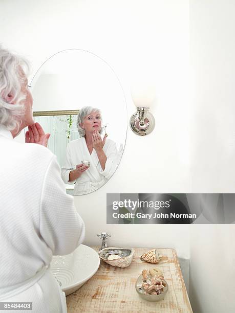 senior applying face cream in mirror - adult in mirror stock-fotos und bilder