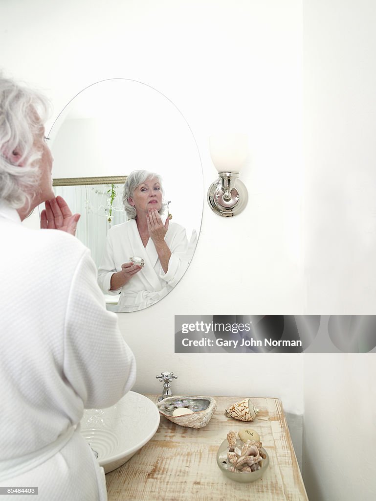 Senior applying face cream in mirror