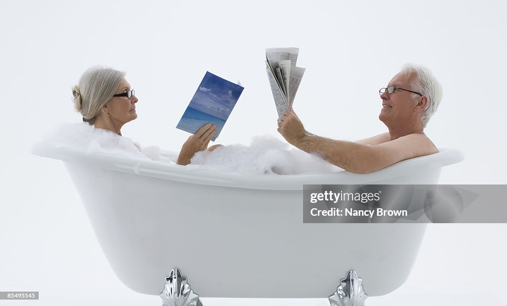 Senior Caucasian Couple in bubble bath reading