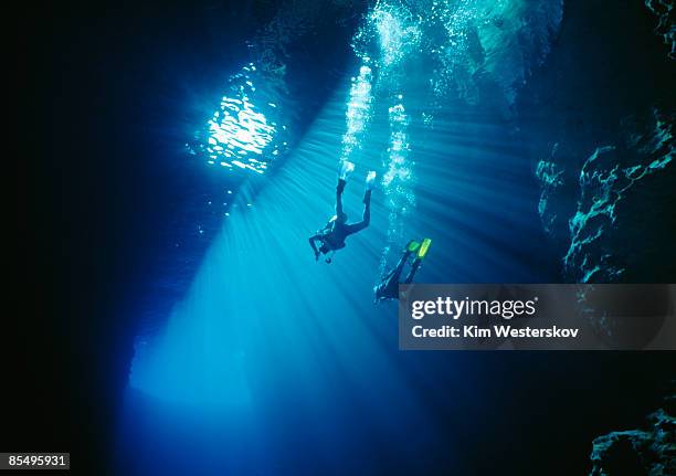 two divers swim thru sunbeams in sea cave, tonga   - isole vavau foto e immagini stock