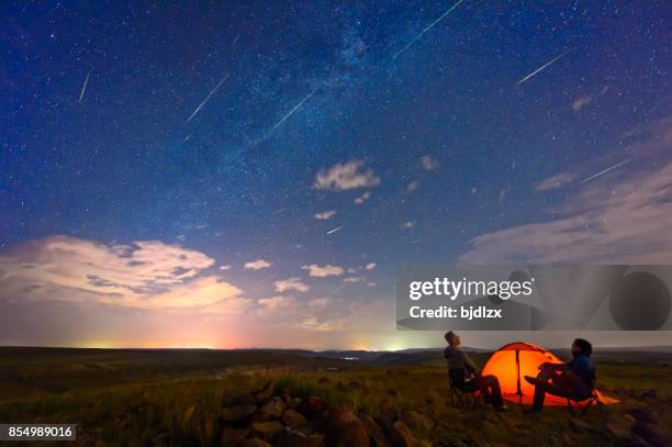 dos hombres están viendo la lluvia de meteoros perseidas, en el borde de la tienda. - perseidas fotografías e imágenes de stock