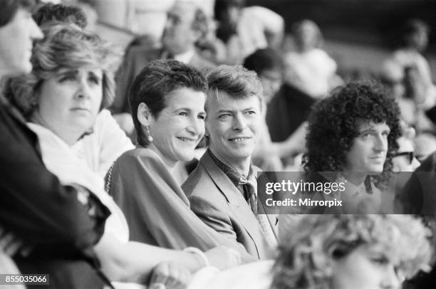 David Bowie and his PA, Corinne 'Coco' Schwab sitting next to Queen guitarist Brian May at the Live Aid benefit concert at Wembley Stadium, London,...