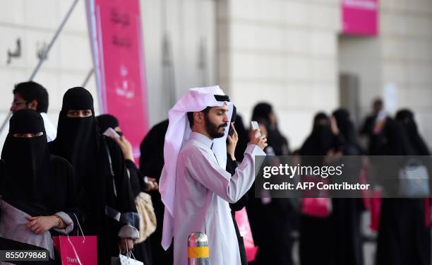 Saudi man checks his mobile as women wait for their drivers outside a hotel in the Saudi capital Riyadh, on September 28, 2017. Saudi Arabia will...