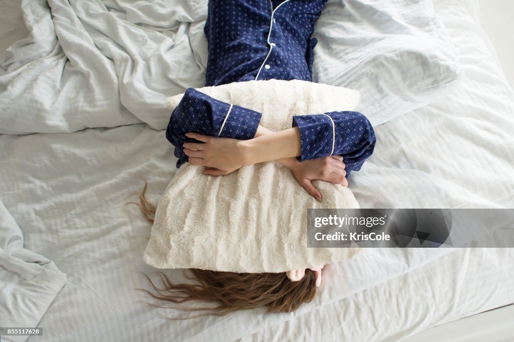 Zu faul, um aus dem Bett, deckt eine Frau ihr Gesicht mit einem Kissen