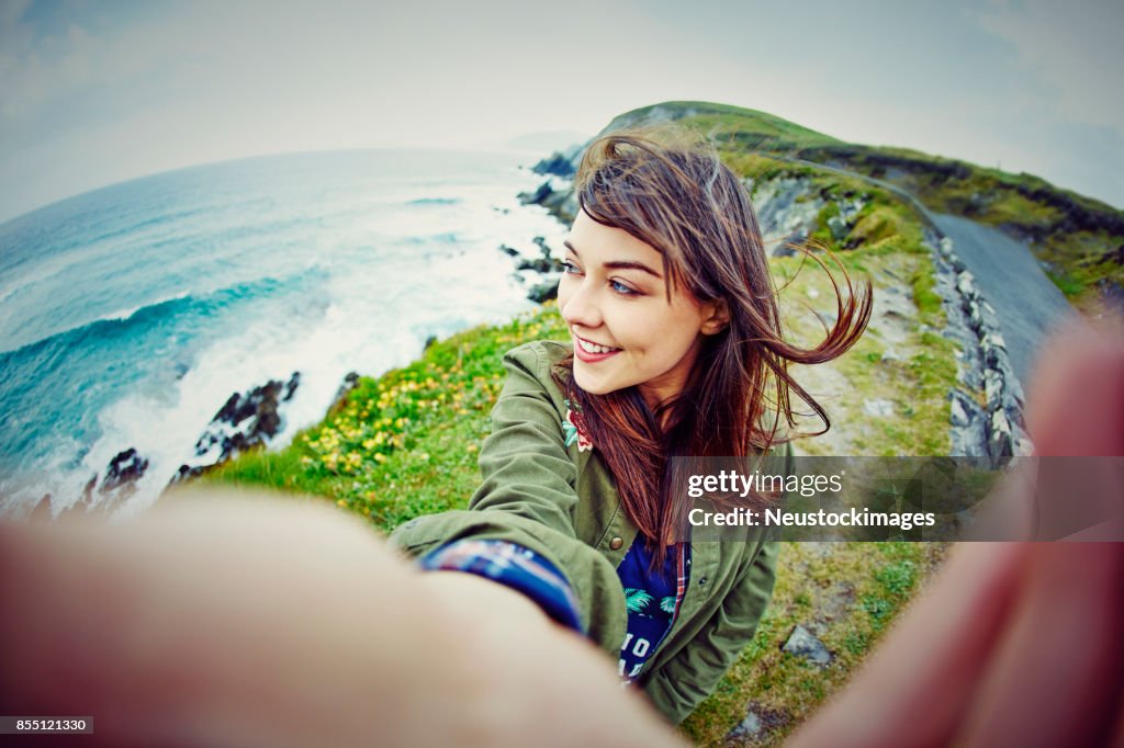 Fish-eye lens of woman taking selfie on mountain by sea