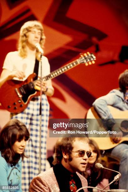 English singer and pianist Elton John performs at a grand piano on the set of a pop music television show in London in April 1972. Visible behind are...