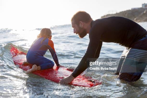 father teaches his little daughter surfing. - surfer wetsuit stockfoto's en -beelden