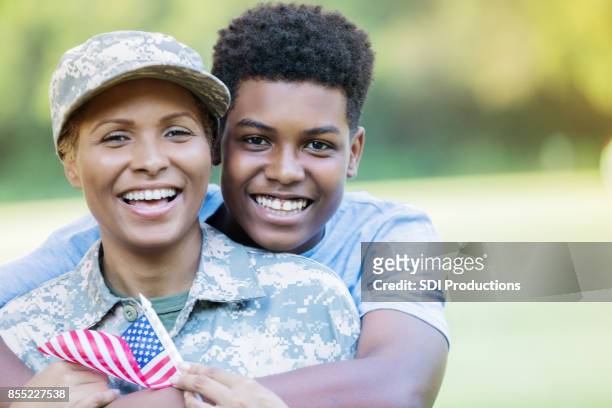 sohn im teenageralter und militärische mutter lächeln für die kamera während der wiedervereinigung - black family reunion stock-fotos und bilder
