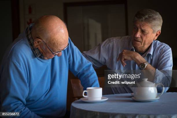 two senior men consoling one another over a cup of coffee - one friend helping two other imagens e fotografias de stock