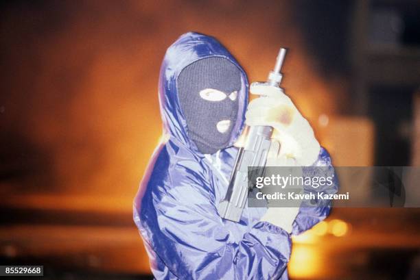 Provisional IRA gunman stands with his automatic assault rifle and a mask after having hijacked and set ablaze a bus on the eve of Apprentice Boys...