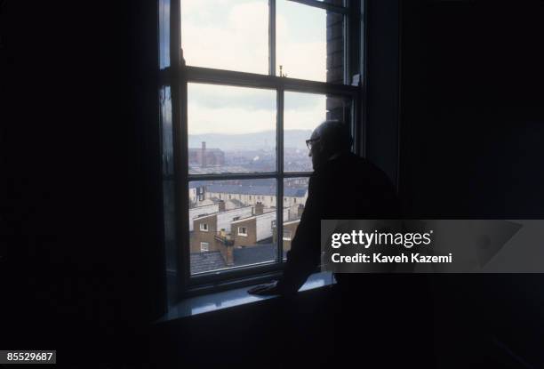 Catholic priest looks out onto the Protestant neighborhoods of west Belfast from a upper floor church window in Falls Road, 18th September 1985.