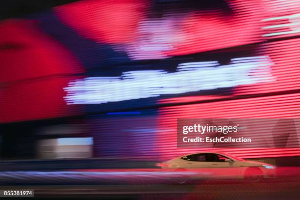 luxury car passing enormous led screen in hong kong - auto rot stock-fotos und bilder