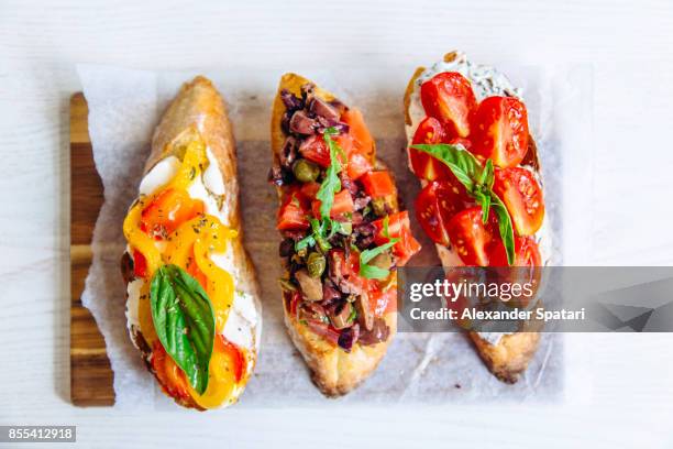 directly above close up shot of bruschettas with tomato, basil, capers, bell pepper and cheese - bruschetta fotografías e imágenes de stock