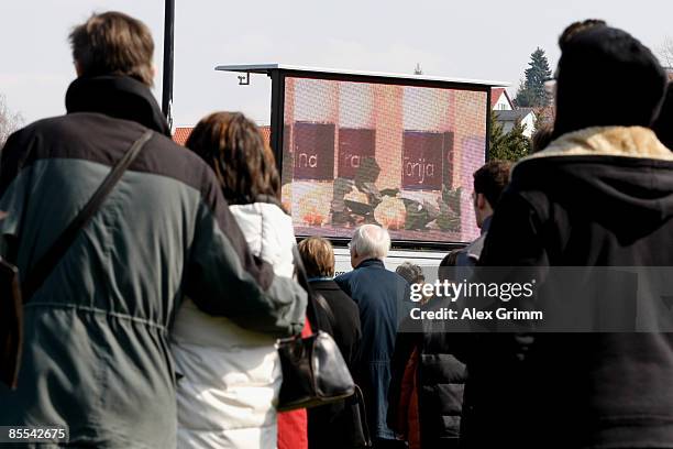 Mourners follow a church service on video screens at a sports field near Albertville high school on March 21, 2009 in Winnenden near Stuttgart,...