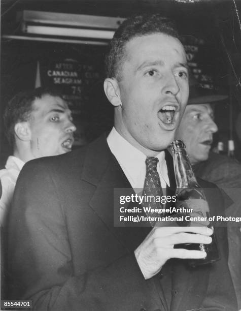 Young man, with open mouth, holding a bottle of beer at a bar, New York, 1946.