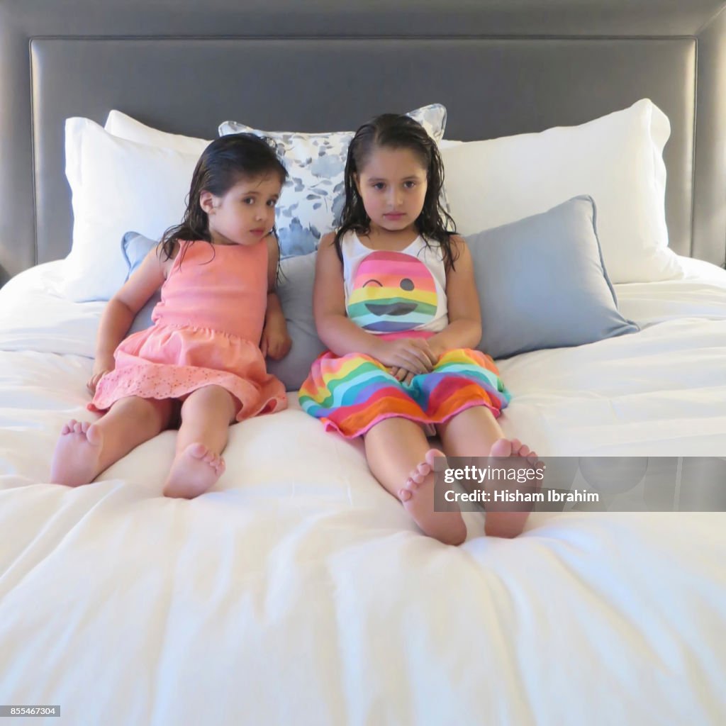 Portrait of two sisters 3 years and 5 years old watching TV in bed, Washington DC, USA.