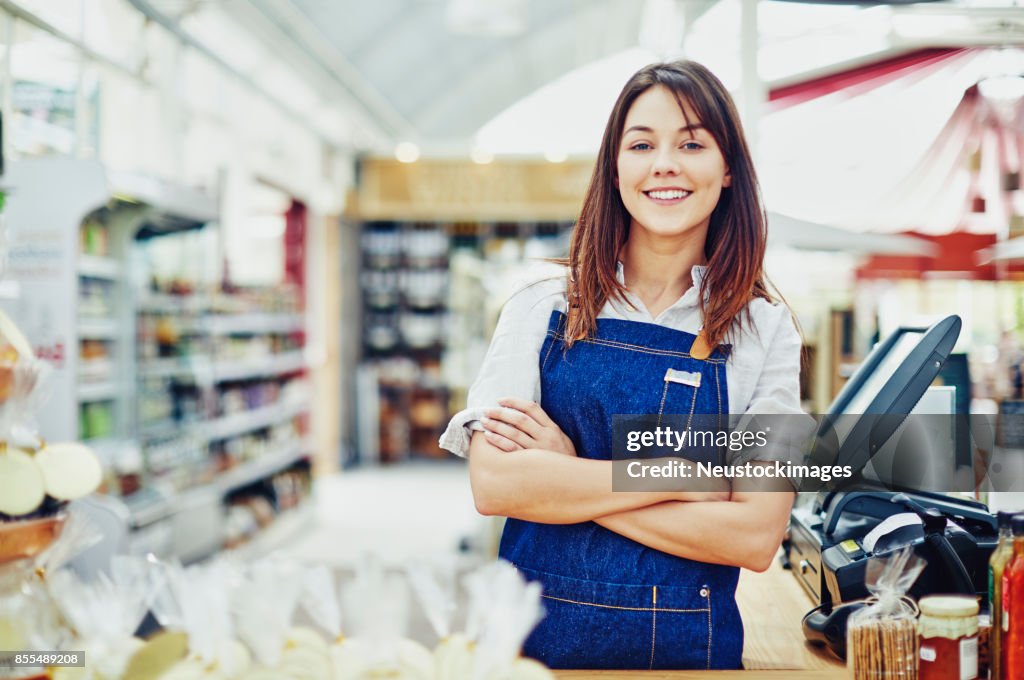 Portrait of confident deli owner standing at checkout counter