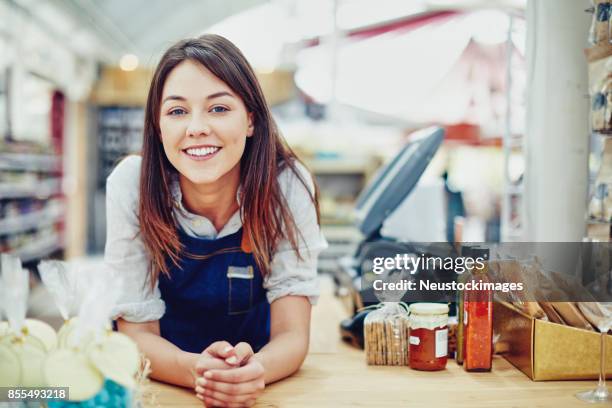 portrait of confident deli owner leaning on checkout counter - loja de conveniencia imagens e fotografias de stock