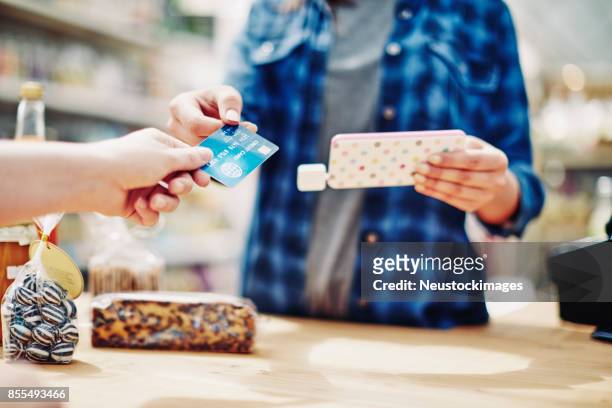 eigentümer halten handys während des empfangs kreditkarte vom kunden - convenience store counter stock-fotos und bilder