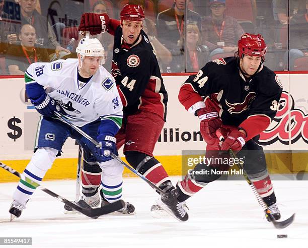Daniel Winnik of the Phoenix Coyotes goes after a rebound as teammate Kurt Sauer fights for position with Pavol Demitra of the Vancouver Canucks in...