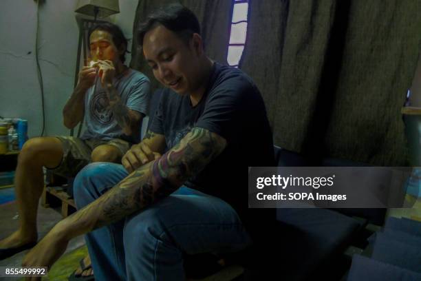 Gary Jones is seen lighting up a cigarette after finishing the tattoo session as the client observed his new tattoo. Gary Jones is one of the Kadazan...