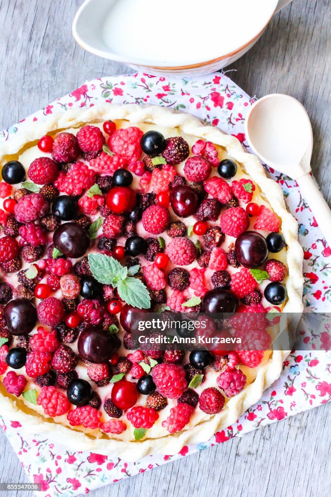 Homemade puff pastry sweet pie with fresh cherry, raspberry, black currant and strawberry with cream cheese decorated with fresh mint on a wooden table, selective focus