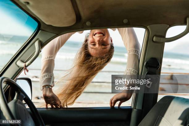 young woman peering down into car window - automobile and fun fotografías e imágenes de stock