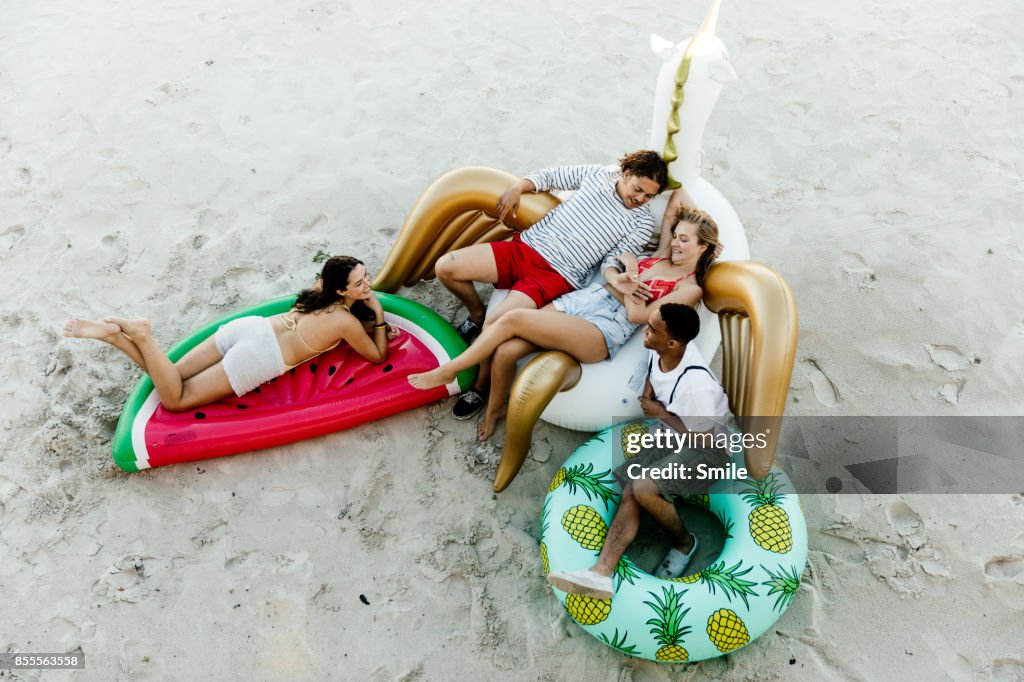 Friends chatting on inflatable toys on the beach