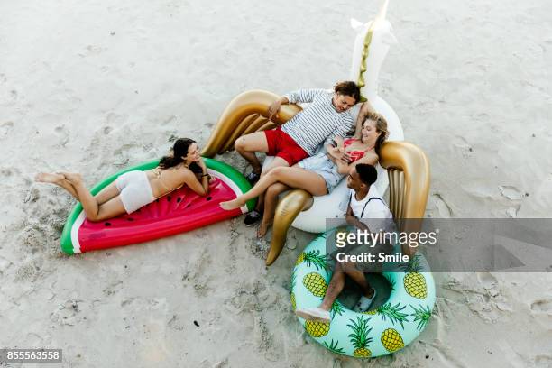 friends chatting on inflatable toys on the beach - african travel smile foto e immagini stock