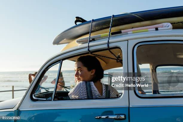young woman looking out car window, surfboards on roof - car top view photos et images de collection