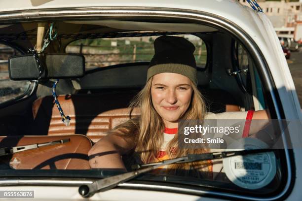 young woman sitting in car smiling - cool cars ストックフォトと画像